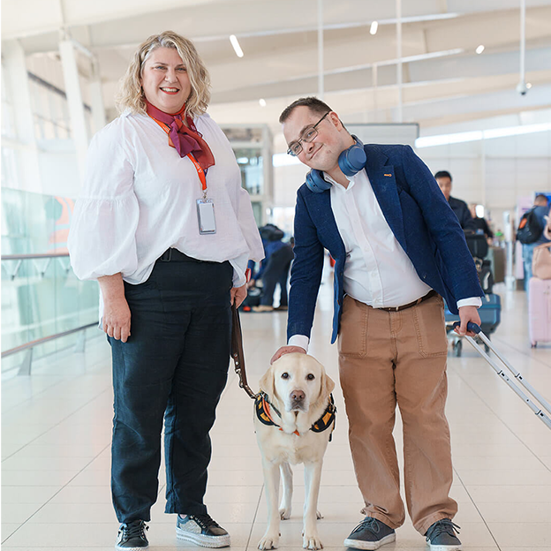 female standing with support dog on lead with male customer patting dog and smiling at camera